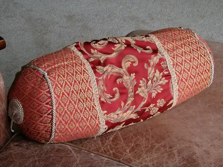 A red damask cushion with a cream embroidered band resting on a sofa